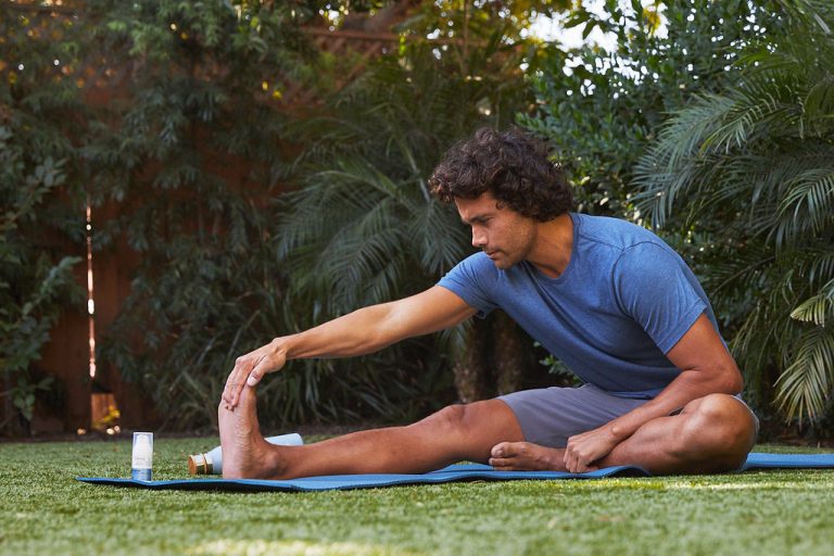Male Yogi stretching with relief cream outdoors in a park