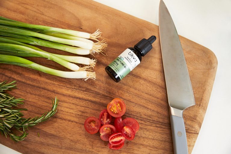 Tikva CBD Tincture Oil on Kitchen Cutting Board with Chives, Herbs, Knife, and Tomatoes